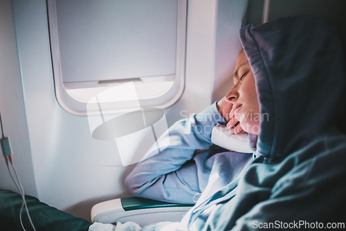 Image of Tired blonde casual caucasian woman wearing sporty hoodie napping on seat while traveling by airplane. Commercial transportation by planes. Authentic image of real people.