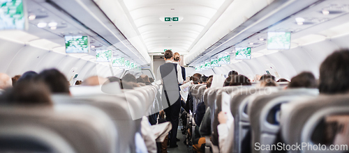 Image of Interior of airplane with passengers on seats and stewardess in uniform walking the aisle, serving people. Commercial economy flight service concept.