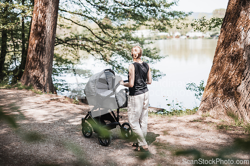 Image of A woman strolling by the lake with a wheeling baby carriage amidst nature