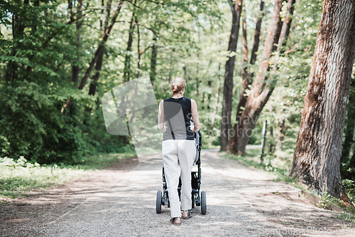 Image of Rear view of casually dressed mother walking with baby stroller in Koseski bajer city park in Ljubljana, Slovenia. Family, child and parenthood concept.
