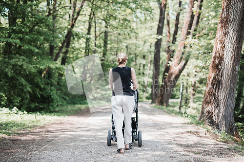 Image of Rear view of casually dressed mother walking with baby stroller in Koseski bajer city park in Ljubljana, Slovenia. Family, child and parenthood concept.