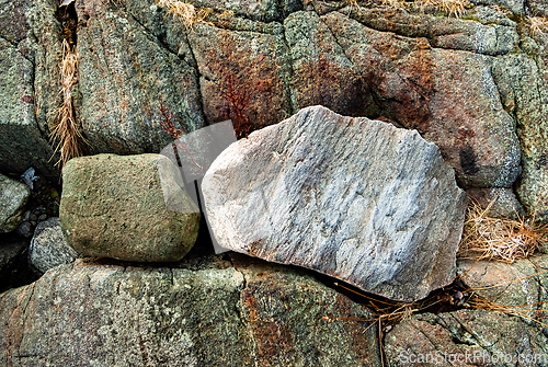 Image of Two unique stones resting on textured rocks beside a gentle tide