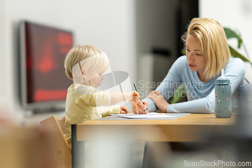Image of Caring young Caucasian mother and small son drawing painting in notebook at home together. Loving mom or nanny having fun learning and playing with her little 1,5 year old infant baby boy child.
