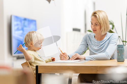 Image of Caring young Caucasian mother and small son drawing painting in notebook at home together. Loving mom or nanny having fun learning and playing with her little 1,5 year old infant baby boy child.