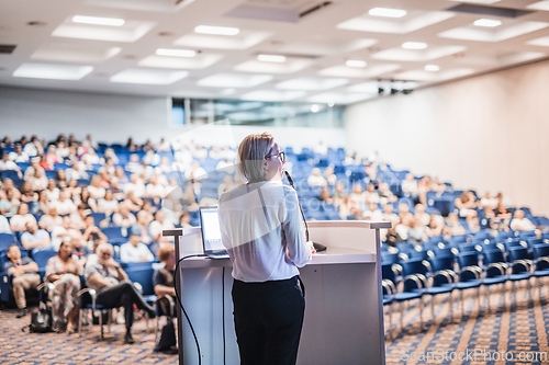 Image of Female speaker giving a talk on corporate business conference. Unrecognizable people in audience at conference hall. Business and Entrepreneurship event.
