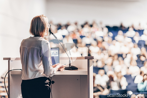 Image of Female speaker giving a talk on corporate business conference. Unrecognizable people in audience at conference hall. Business and Entrepreneurship event.