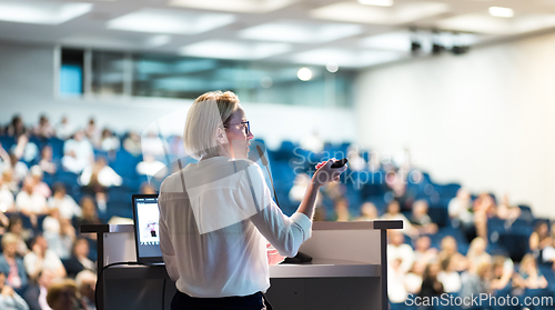 Image of Female speaker giving a talk on corporate business conference. Unrecognizable people in audience at conference hall. Business and Entrepreneurship event.