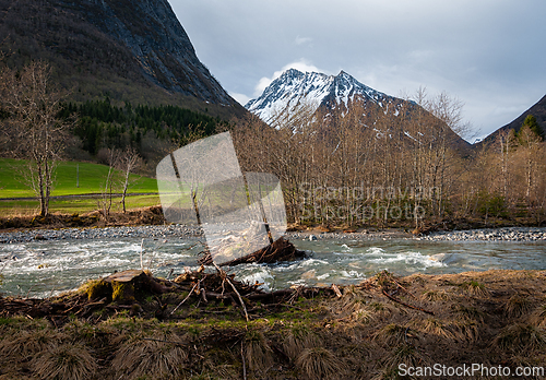 Image of A serene river flows past winter-bare trees with snow-capped mou