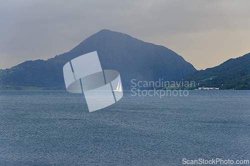 Image of A lone sailboat glides across the calm waters of a serene fjord 