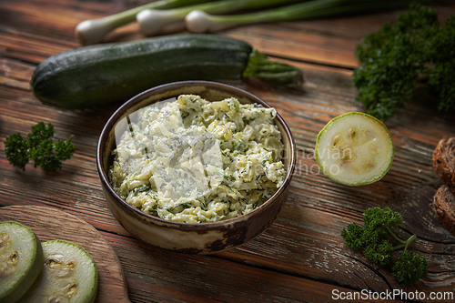 Image of Bowl of zucchini spread is surrounded by fresh zucchini slices,