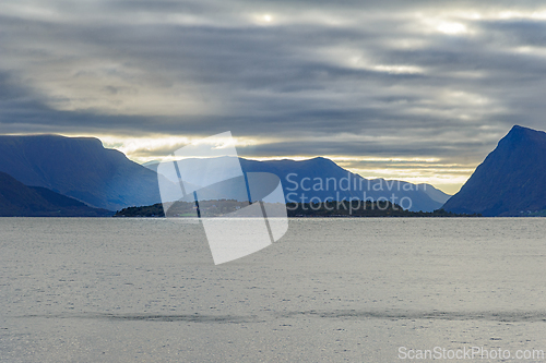 Image of Tranquil waters reflect mountainous landscape at dawn near an is