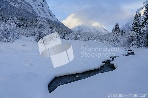 Image of A tranquil winter landscape featuring a snow-covered stream and 