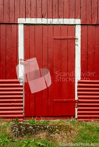 Image of A weathered red barn door framed by white trim and corrugated me