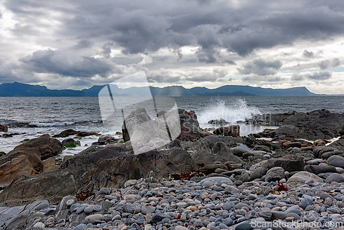 Image of Waves crash against rocky shore under a dramatic sky at the coas