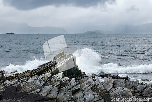 Image of Waves crash against rugged coastal rocks under a dramatic sky at