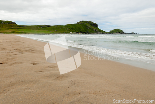 Image of A tranquil beach stretches along a rugged coastline, with gentle
