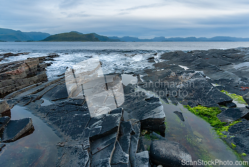 Image of Vast rocky shoreline at twilight, reflecting calm waters and dis