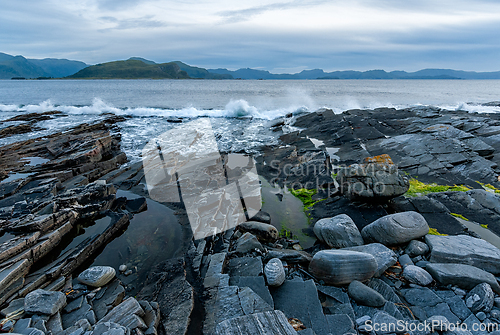 Image of Waves crashing against rocky shorelines at dusk, revealing the s
