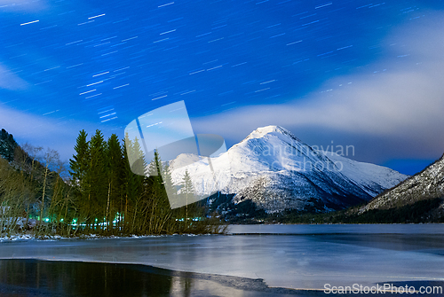 Image of Snow-covered mountain under a starry night sky beside a frozen l