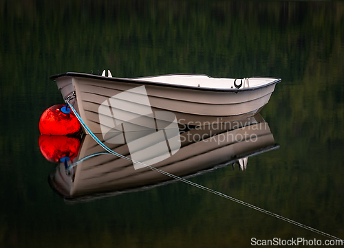 Image of A small boat is docked in a calm lake, its reflection perfectly 