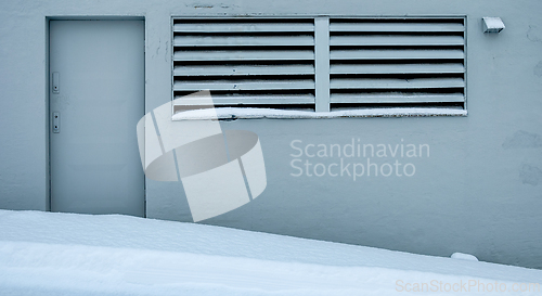 Image of A gray door with two handles is next to a slatted window on a gr