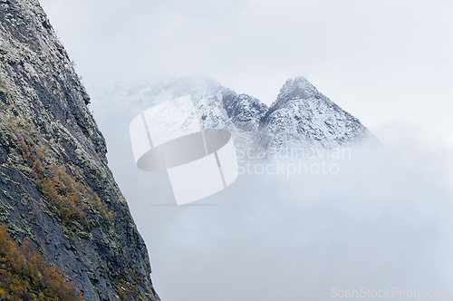 Image of A rocky cliff juts out towards a snowy mountain range partially 
