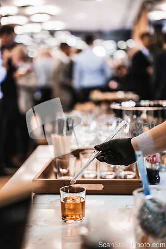 Image of Expert barman is making cocktail at business banquet event in hotel conference center. Blurred businesspeople at banquet event business meeting event in the background