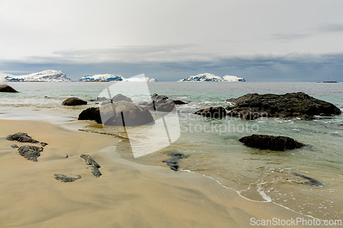Image of A sandy beach with large rocks and small waves near snow-capped 