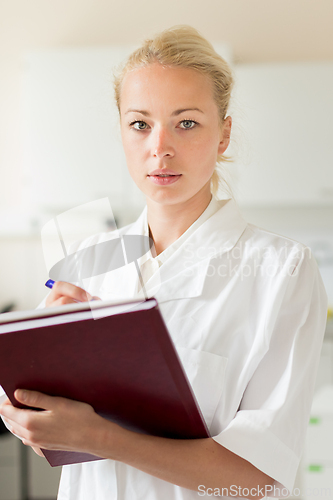 Image of Portrait of young, confident female health care professional taking notes during inventory in scientific laboratory or medical doctors office