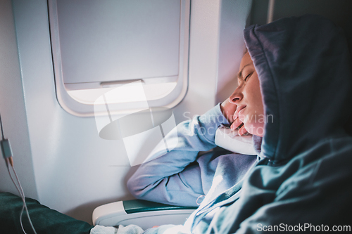 Image of Tired blonde casual caucasian woman wearing sporty hoodie napping on seat while traveling by airplane. Commercial transportation by planes. Authentic image of real people.