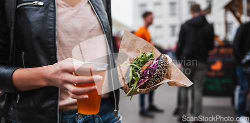 Image of Close up of woman hands holding delicious organic salmon vegetarian burger and homebrewed IPA beer on open air beer an burger urban street food festival in Ljubljana, Slovenia.