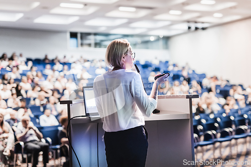 Image of Female speaker giving a talk on corporate business conference. Unrecognizable people in audience at conference hall. Business and Entrepreneurship event.