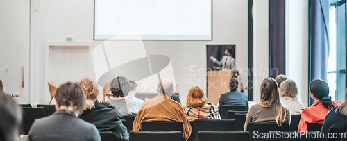 Image of Speaker giving a talk in conference hall at business event. Rear view of unrecognizable people in audience at the conference hall. Business and entrepreneurship concept.