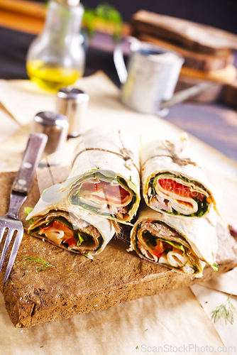 Image of Sliced sandwich tortilla with tomatoes , salad , cream cheese and ham .