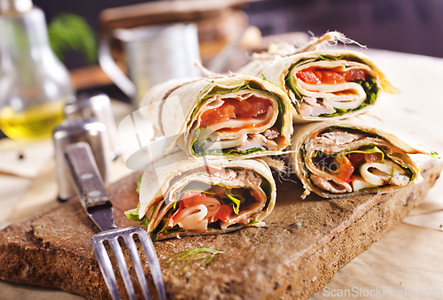 Image of Sliced sandwich tortilla with tomatoes , salad , cream cheese and ham .