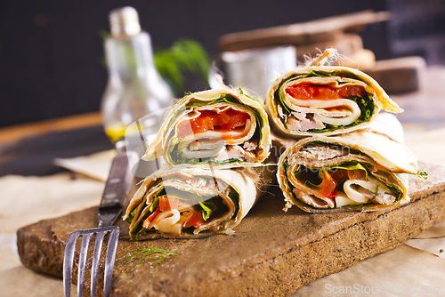 Image of Sliced sandwich tortilla with tomatoes , salad , cream cheese and ham .