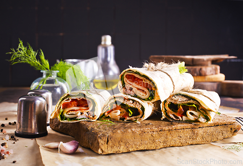 Image of Sliced sandwich tortilla with tomatoes , salad , cream cheese and ham .
