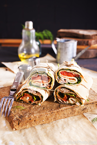 Image of Sliced sandwich tortilla with tomatoes , salad , cream cheese and ham .