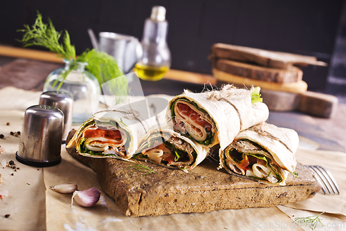 Image of Sliced sandwich tortilla with tomatoes , salad , cream cheese and ham .