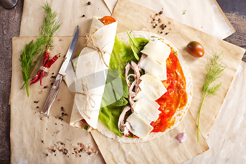 Image of Sliced sandwich tortilla with tomatoes , salad , cream cheese and ham .