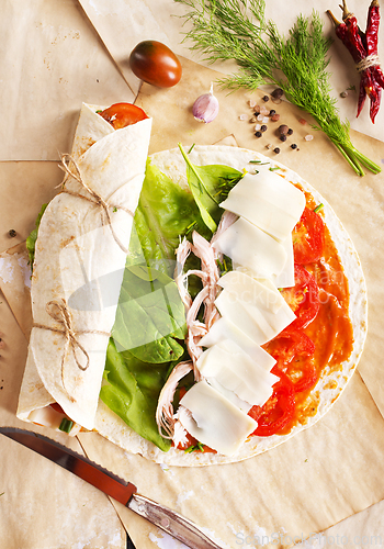 Image of Sliced sandwich tortilla with tomatoes , salad , cream cheese and ham .