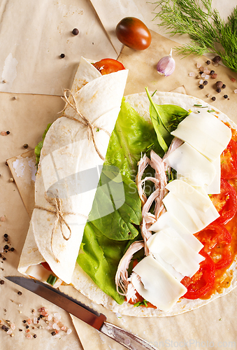 Image of Sliced sandwich tortilla with tomatoes , salad , cream cheese and ham .