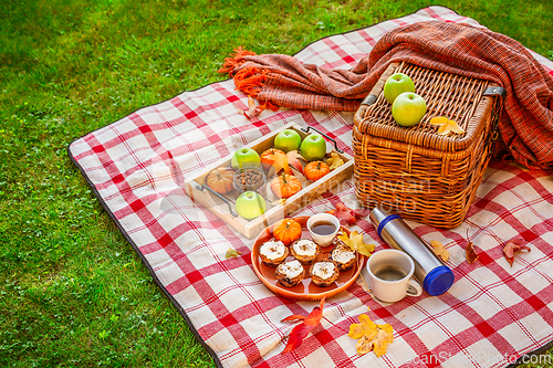 Image of Autumn picnic in a park with pumpkin cupcakes and muffins, coffee and tea