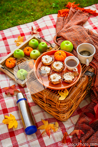 Image of Autumn picnic in a park with pumpkin cupcakes and muffins, coffee and tea