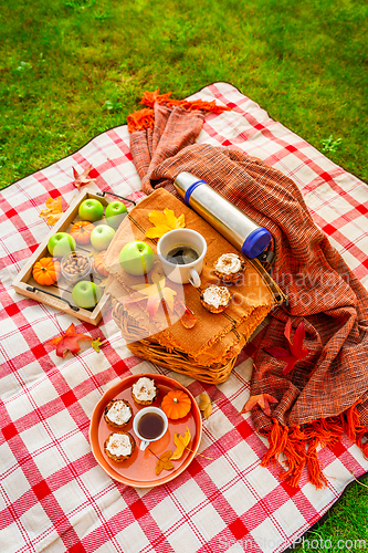Image of Autumn picnic in a park with pumpkin cupcakes and muffins, coffee and tea
