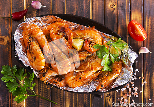Image of Roast Prawns Shrimps in a pan with herbs and garlic. Dark wooden background.