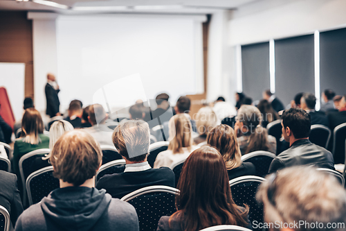 Image of Speaker giving a talk in conference hall at business event. Rear view of unrecognizable people in audience at the conference hall. Business and entrepreneurship concept.