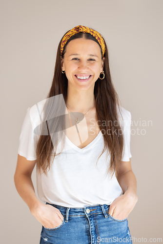 Image of Portrait of confident beautiful woman with long brown hair, wearing casual clothes, standing in relaxed pose with hands in pockets, smiling with white teeth at camera, studio background.