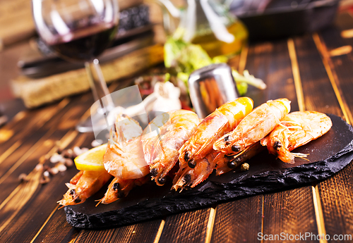 Image of Fried shrimps with garlic, lemon served on black plate on wooden table