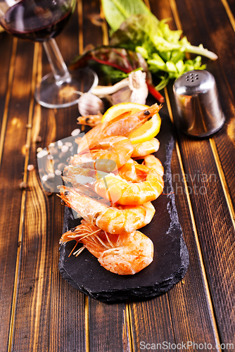 Image of Fried shrimps with garlic, lemon served on black plate on wooden table